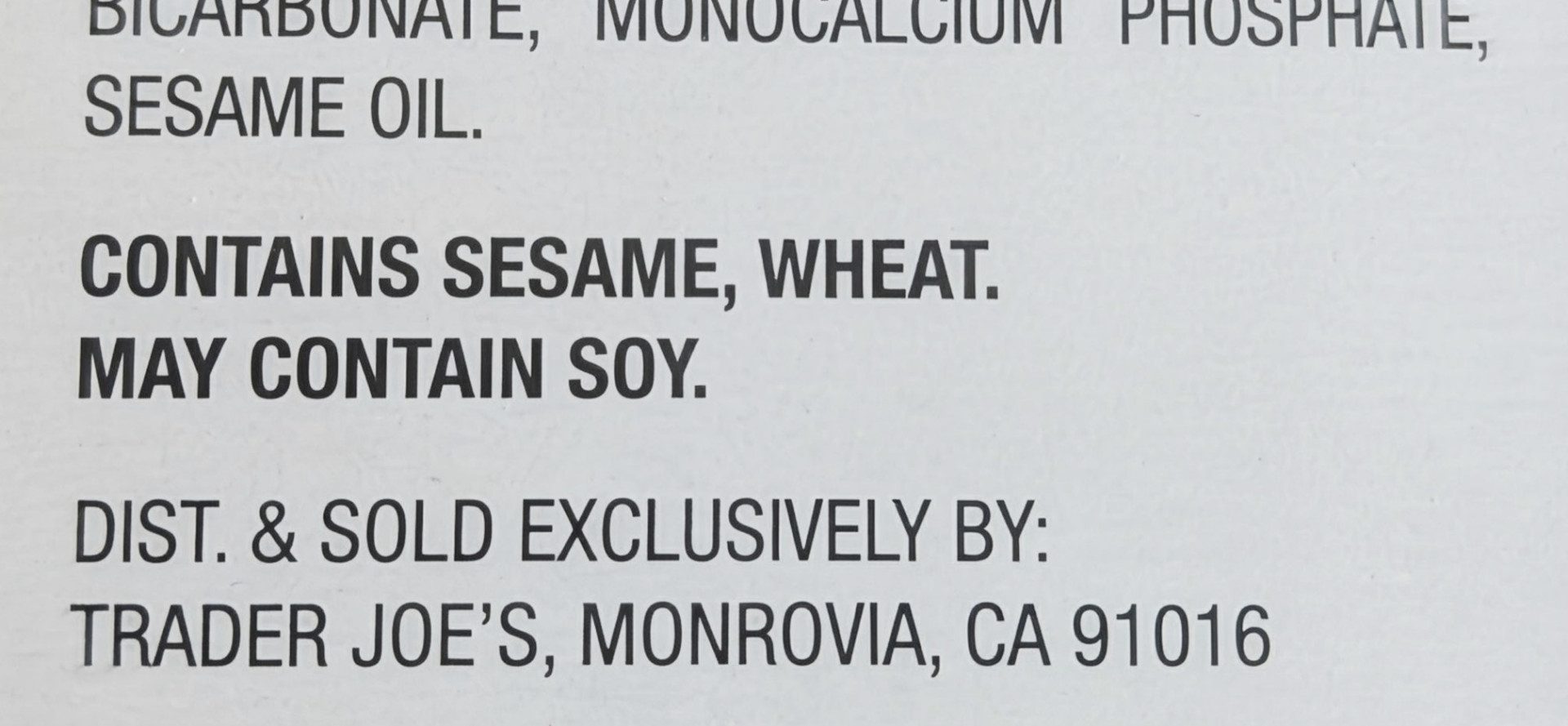 Close-up of a grocery packaging label with a bold 'Contains sesame, wheat. May contain soy.' precautionary allergen statement